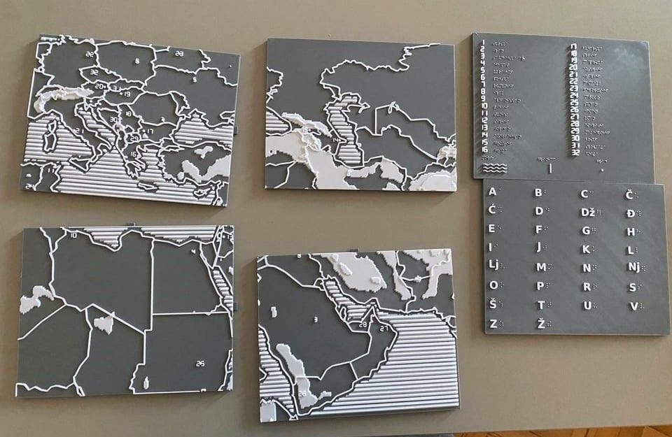 All six printed pieces laid out together on a table: four map tiles, the braille legend card and the braille alphabet card with raised Serbian letters beside each cell.